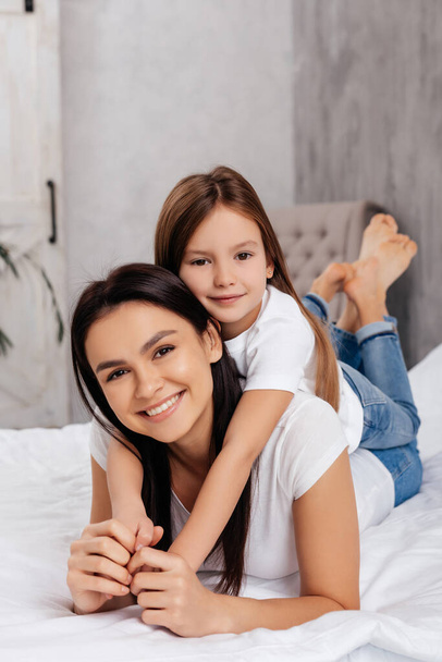 Gorgeous positive female relaxing with her lovely daughter on comfortable bed - Fotografie, Obrázek