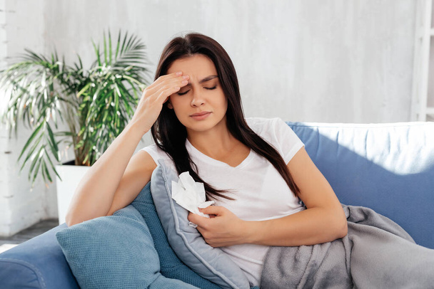 Worried female touching her forehead and keeping eyes closed while resting on sofa - Photo, image