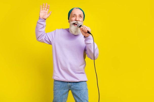 Photo of positive attractive mature man dressed purple pullover singing karaoke rising arm isolated yellow color background - Fotó, kép