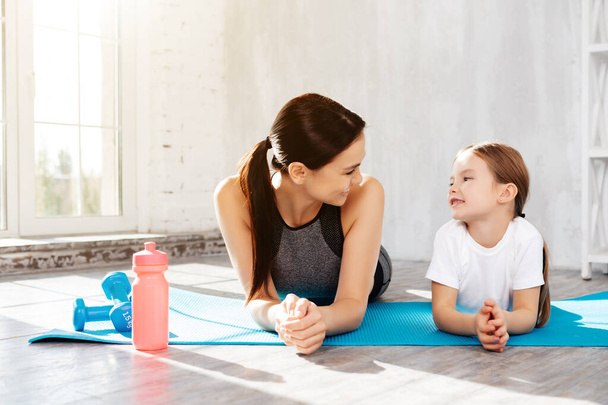 Delighted woman looking at her child with love while resting on fitness mat - Foto, imagen