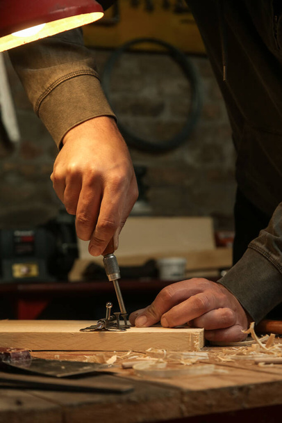 Carpintero atornillando bisagras de metal cromado en tablón de madera en el taller. - Foto, Imagen