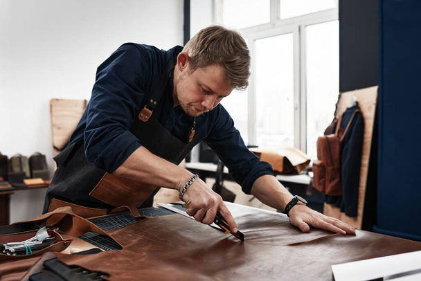 leather craftsmen working making measupenets in patterns at table in workshop studio - Foto, Bild