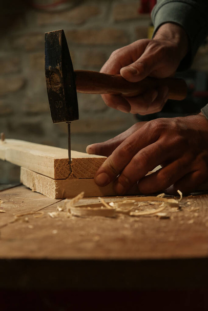 Tesař zabodává hřebík do dřevěné desky v dílně. - Fotografie, Obrázek