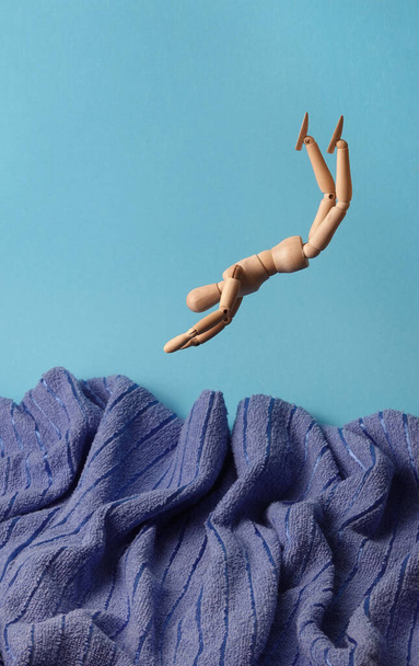    Hombre de madera dibujo maniquí figura modelo concepto está saltando en agua turbulenta toalla azul simbólico ondulado océano aislado sobre fondo blanco                             - Foto, imagen
