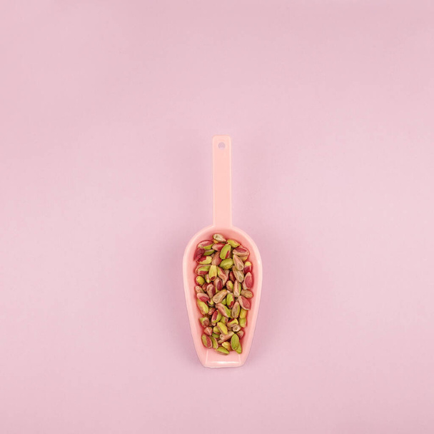 Pistácios descascados kernels em rosa colher de medição sobre fundo rosa quadrado                                 - Foto, Imagem