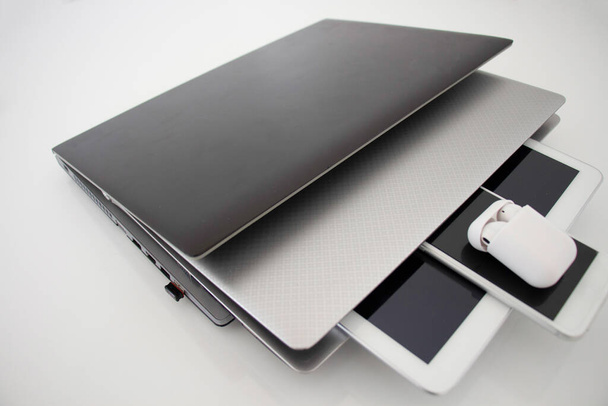 portátil, portátil, tableta, teléfono y auriculares entrelazados y estafa sobre un fondo blanco. Dispositivos de comunicación, - Foto, Imagen
