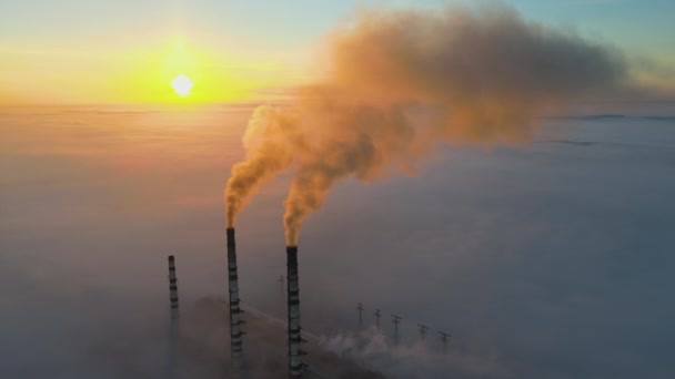 Uitzicht vanuit de lucht op hoge pijpen van kolencentrales met zwarte rook die bij zonsondergang de vervuilende atmosfeer opgaat. - Video