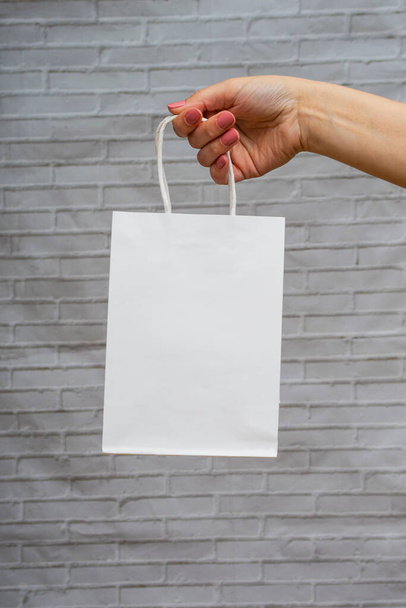 Weiße Paket-Attrappe in Nahaufnahme auf grauem Backsteinhintergrund. Weiße Öko-Verpackung in der Hand einer Frau. Online-Shopping-Konzept - Foto, Bild