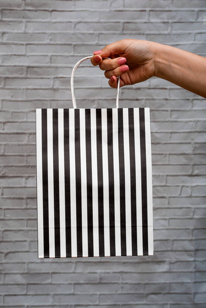 Primer plano maqueta de eco-embalaje sobre un fondo gris ladrillo. Bolso Kraft en rayas blancas y negras en la mano de una mujer. Compras online - Foto, imagen