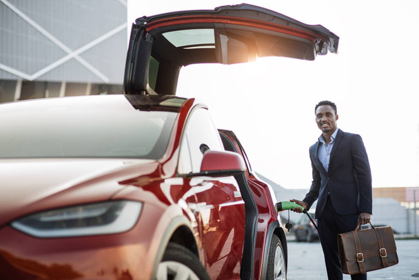 African businessman with suitcase charging electric car - 写真・画像