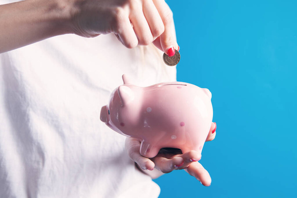 Young woman  putting a coin inside piggy bank as savings for investment - Fotó, kép