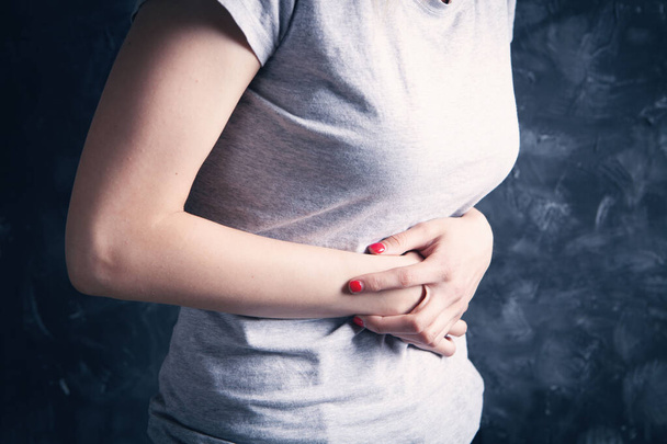 in a young woman, her stomach hurts on a gray background - Photo, image