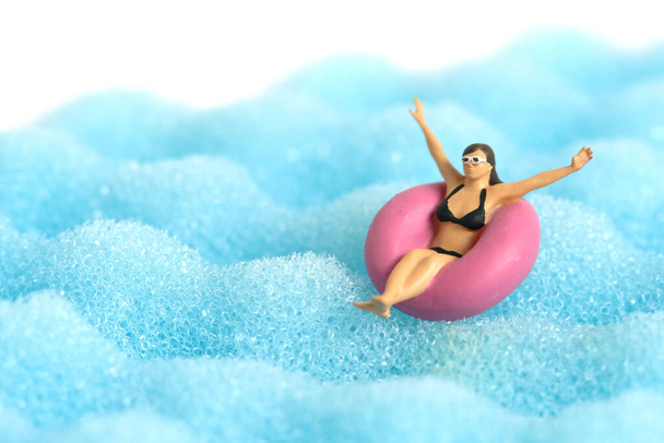Fotografování figurek miniaturních lidí. Dívka v černém slunečním skle plavat s gumovým trubkovým kroužkem na vlnitém oceánu. Fotografie obrázku - Fotografie, Obrázek
