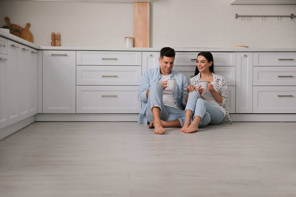 Happy couple sitting on warm floor in kitchen. Heating system - Foto, immagini