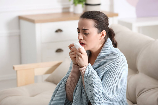 Young woman suffering from runny nose in living room - Fotoğraf, Görsel