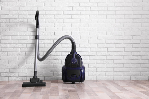 Modern vacuum cleaner near white brick wall indoors - Fotó, kép
