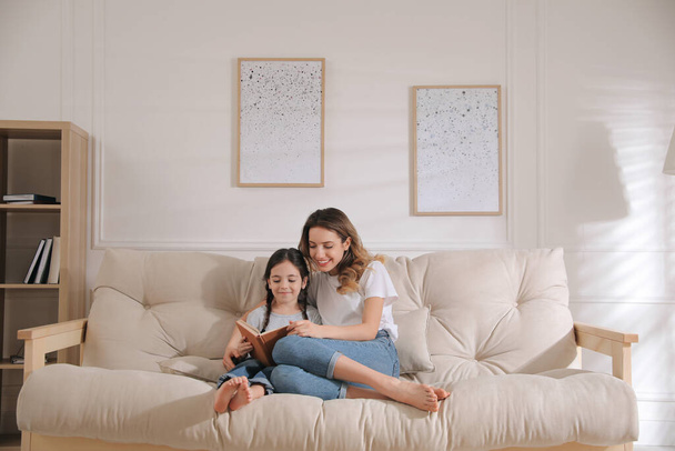Mother and daughter reading book on sofa at home - Photo, image