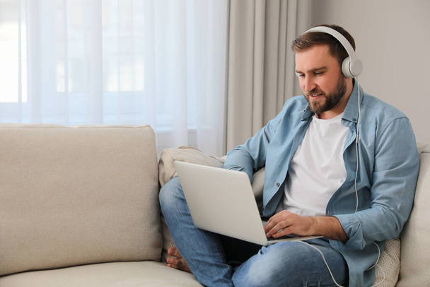 Man with laptop and headphones sitting on sofa at home - Photo, image