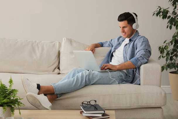 Man with laptop and headphones sitting on sofa at home - 写真・画像