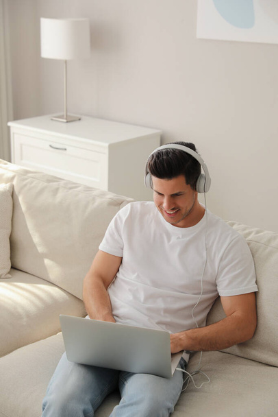 Man with laptop and headphones sitting on sofa at home - Foto, afbeelding