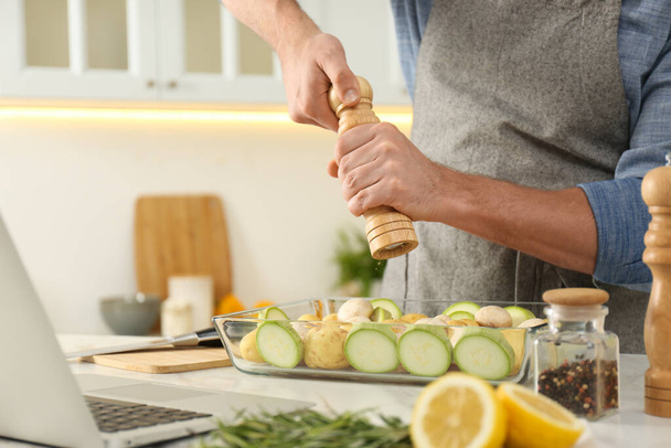 Muž přidání koření k jídlu při sledování online kurzu vaření přes notebook v kuchyni, detailní záběr - Fotografie, Obrázek