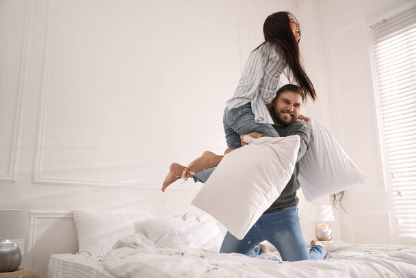 Happy young couple having fun pillow fight in bedroom - Foto, immagini