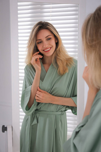 Pretty young woman in beautiful silk robe near mirror at home - Foto, afbeelding