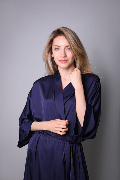 Pretty young woman in beautiful dark blue silk robe on grey background - Photo, image