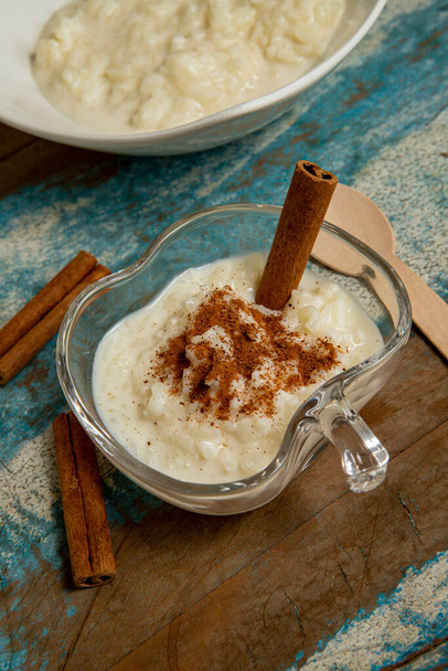 Traditional June party brazilian dessert made of rice and condensed milk called arroz doce decorated with cinnamon on colorful wooden table - Photo, Image