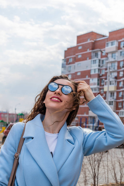 Young woman in mirrored sunglasses looks into the sky. Wellness concept. Adult girl walks and breathes fresh air in the spring. - Foto, afbeelding