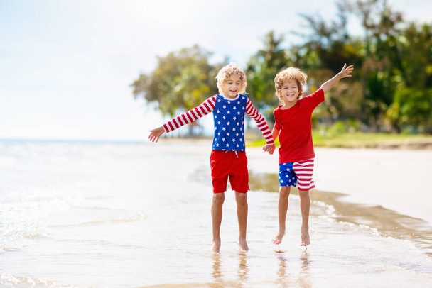 Kids run with USA flag on sunny beach. 4th of July celebration. American family fun on Independence Day weekend. Patriotic children celebrate US holiday. Boy and girl with symbols of America. - Foto, Imagen