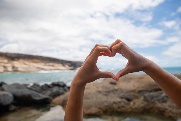 Kalp şeklinde elleri olan bir kızın yaz tatilinin tadını çıkardığı sahili kapatın. Aşk Doğa Konsepti - Fotoğraf, Görsel