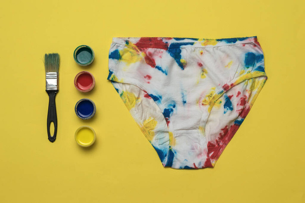 Paint and painted women's panties in the style of tie dye on a yellow background. Colored underwear at home. - Photo, Image