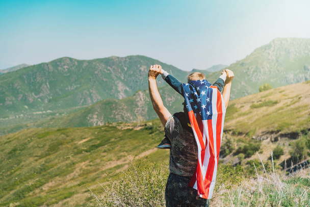 Homme avec un enfant sur le cou, garçon sur le dos a un drapeau américain sur le fond de la nature. - Photo, image