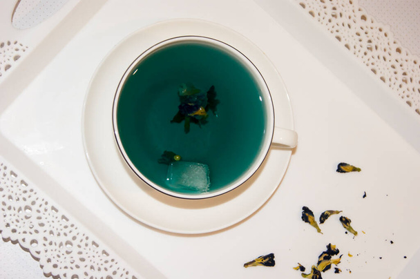 Barva nálady je modrá - modrý čaj v bílém hrnku, který stojí na bílém talíři a bílém tácu. Užitečné nápoje, léčivé vlastnosti. Fytoterapie. Tea party. - Fotografie, Obrázek