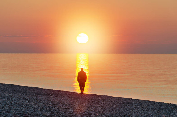 L'uomo si trova di fronte al mare alla luce del sole. Silhouette umana nel flusso di luce solare. Concetto di trovare la tua strada e il senso della vita.  - Foto, immagini