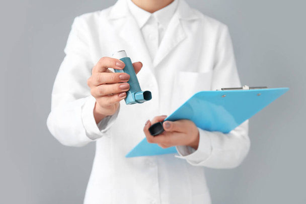 Alergista femenina con inhalador y portapapeles sobre fondo gris - Foto, Imagen