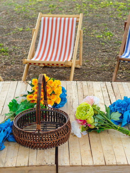 Prachtige kunstmatige boeketten van verschillende kleuren geplaatst op houten tafel tussen ligstoelen in de tuin. Multi-gekleurde kunstbloemen sieren de houten tafel voor mooie en ontspannen. Selectieve focus. - Foto, afbeelding