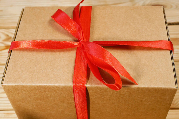 Ajándék csomag doboz szalaggal piros íj, barna karton csomag, meglepetés, közelkép - Fotó, kép