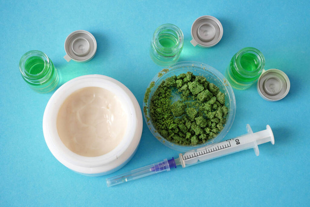Crema di cannabis cosmetica in dose con pianta di marijuana e olio su fondo blu. Concetto di cosmetici a base di cannabis. Primo piano - Foto, immagini