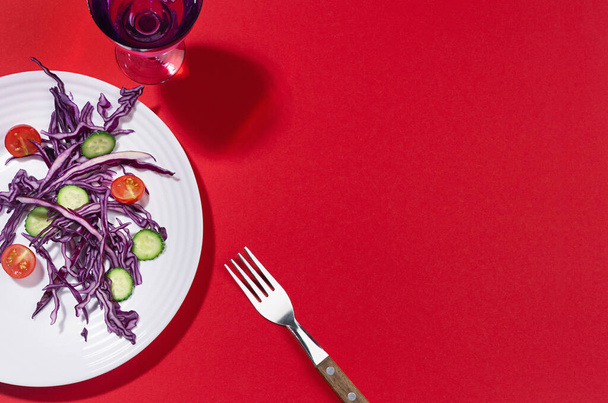 Raw healthy salad in crop white plate with purple cabbage, red tomatoes, cucumber, drink in hard light with shadow on red background. - Photo, image