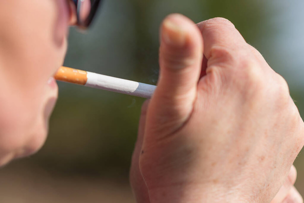 Žena středního věku kouří venku cigarety se sluncem na tváři. Rozmazané pozadí.Portrét postranního pohledu.Telsiai, Litva 01-06-2021 - Fotografie, Obrázek