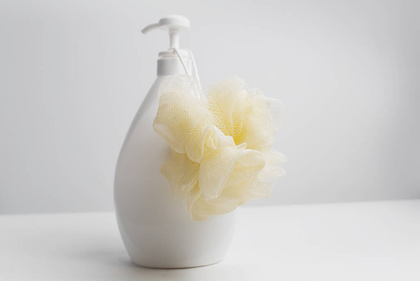 Close-up of yellow washcloth on dispenser bottle against white studio background. - Фото, изображение