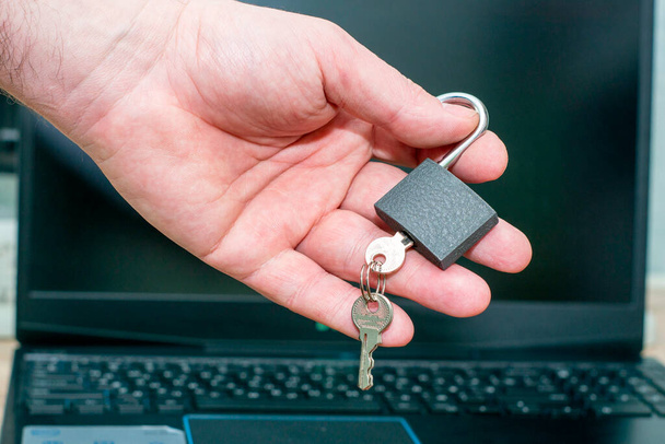 Bir adam elinde anahtarlarıyla bir dizüstü bilgisayarın arka planına karşı açık bir asma kilit tutuyor. İnternet sansürü kavramı. Yüksek kalite fotoğraf - Fotoğraf, Görsel