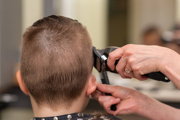 Cute kid boy have hair cut, professional barber doing haircut. Hairdress for children. Kid side view portraits in the barbershop.Back view. - Photo, Image