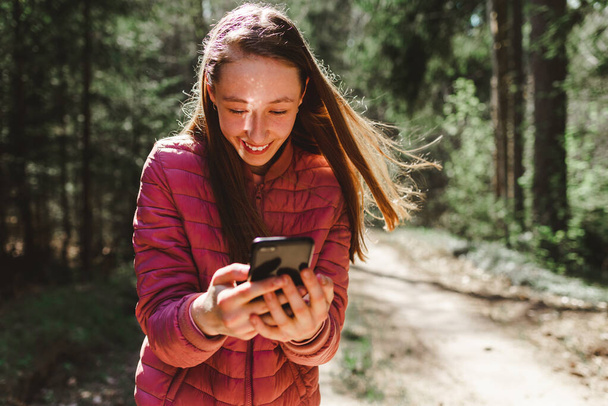 Une fille de 13 ans faisant un appel vidéo à son ami dans la forêt, Concept de communication en ligne.Belle journée ensoleillée de printemps ou d'été. - Photo, image