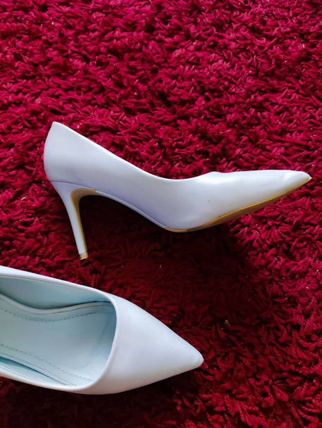 A vertical shot of a pair of white classic high heels on a fluffy red rug - Fotografie, Obrázek