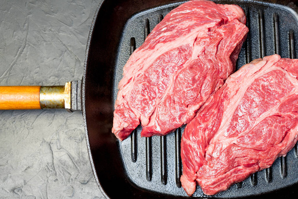 A raw marbled beef steak sits in a frying pan. - Fotografie, Obrázek