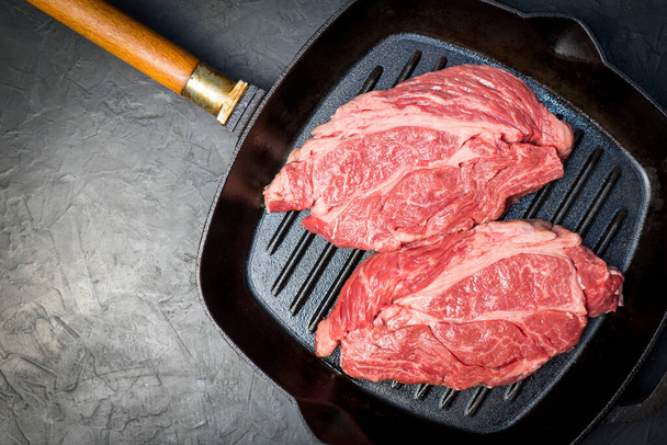 A raw marbled beef steak sits in a frying pan. - Fotografie, Obrázek