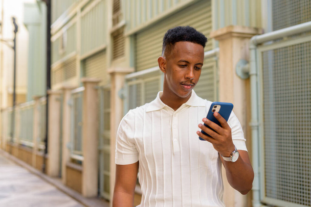 Portrait of confident young African businessman wearing casual clothes and using mobile phone - Foto, afbeelding